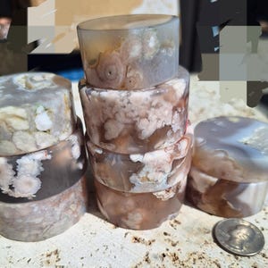 May include: A collection of cylindrical stone objects in shades of brown, gray, and white. The objects are stacked and arranged, showcasing unique patterns and textures. A quarter coin is visible near the objects.