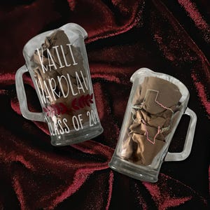 May include: Two clear glass pitchers with handles, filled with brown paper. One pitcher has the text "KAILI WARDLAW CLASS OF 20--" and a floral design. The other pitcher has a Texas outline and the word "home".