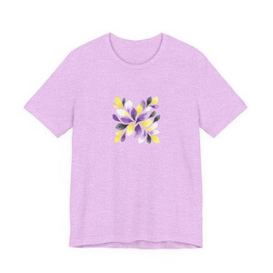 May include: A pale lilac t-shirt with a floral design. The design features yellow, purple, white, and black leaf-like shapes arranged symmetrically. The shirt has short sleeves and a crew neck.