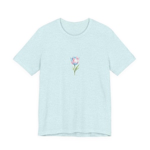 May include: Pale blue t-shirt with a watercolour tulip design. The tulip has pink and blue petals, green leaves and stem. The shirt is made of a soft, heathered fabric.