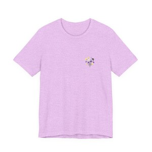 May include: A light purple t-shirt with a small floral design on the left chest. The floral design includes purple, yellow, and white flowers. The t-shirt has short sleeves and a crew neck.