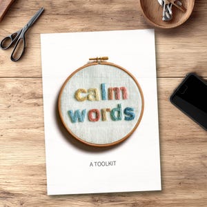 Könnte beinhalten: Ein weißes Poster mit einem Stickrahmen, der die Worte "calm words" in farbigem Garn zeigt. Der Text "A TOOLKIT" steht darunter. Schere, Schlüssel und ein Telefon liegen auf einer Holzoberfläche.