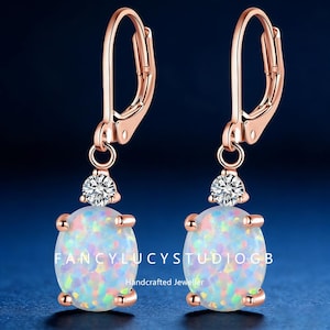 May include: Rose gold leverback earrings with oval opal stones and a small diamond accent. The earrings have the text "FancylucystudioGB Handcrafted Jeweller". The opal stones have a colorful, iridescent appearance.
