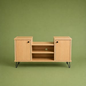 May include: A light wood media console featuring two side cabinets with small black circular knobs and a central open section with two shelves. The unit is supported by four thin black metal hairpin legs and includes a circular cable cutout.