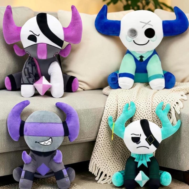 May include: Four plush toys with unique designs. Each has a white head, horns, and a distinctive outfit. The toys feature various colors, including purple, blue, teal, and gray. They are sitting on a beige couch with a white blanket.