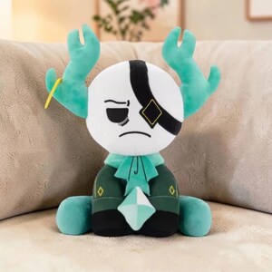 May include: A plush doll with a white head, black eye mask, and teal antlers. The doll wears a teal and green outfit with a diamond-shaped gem. The doll is sitting on a beige surface.