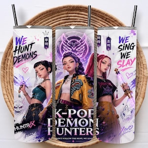 May include: Three cylindrical tumblers with black straws featuring anime-style characters and text. The designs include the phrases "WE HUNT DEMONS," "K-POP DEMON HUNTERS," and "WE SING WE SLAY" alongside purple and yellow accents, hearts, and masks.