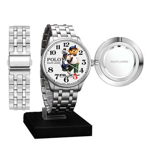 May include: A silver wristwatch with a white face featuring a Polo bear graphic. The watch has a stainless steel band and a separate band piece. The watch face displays the Polo Ralph Lauren logo and the text "RLX". The watch is displayed on a black stand.
