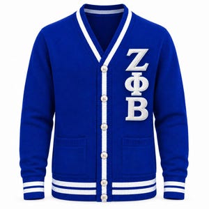 May include: A royal blue V-neck cardigan sweater featuring white striped trim on the cuffs, hem, and button placket. The front displays large white embroidered Greek letters ZΦB on the left chest and includes two front pockets with buttons.