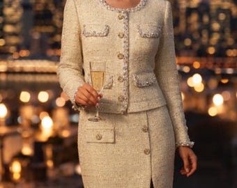 May include: Cream-colored tweed skirt suit with pearl and rhinestone embellishments. The jacket has a round neckline, four pockets, and decorative buttons. The skirt features a front slit and matching buttons. A champagne flute is held in the hand.