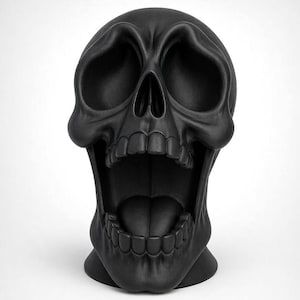 Puede incluir: Una escultura de cráneo negro mate que presenta una boca exageradamente abierta con dientes y lengua visibles. El cráneo tiene cuencas oculares profundas y huecas, con una textura de superficie lisa y uniforme, en posición frontal.