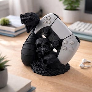 Könnte beinhalten: Ein schwarz-weißer PlayStation 5-Controller ruht auf einem schwarzen Controller-Ständer im Schädel- und Schlangen-Design. Der Ständer zeigt einen detaillierten Schlangenkopf und mehrere Schädel. Der Controller ist weiß mit schwarzen Akzenten.