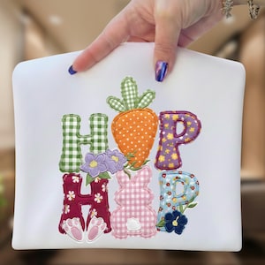 Könnte beinhalten: Weißer Stoff mit dem Wort "HOP" in bunten, applizierten Buchstaben. Das "H" ist grün-kariert, das "O" ist eine orangefarbene Karotte und das "P" ist lila mit gelben Blumen. Das "H" ist bordeauxfarben mit weißen Blumen und Hasenpfoten, und das "P" ist blau mit Blumen.