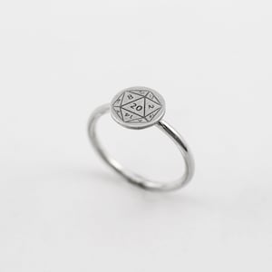 May include: A silver ring with a round, engraved design of a twenty-sided die. The die has numbers 2, 4, 6, 8, 10, 12, 14, 16, 18, 20, 12, 10, 8, 6, 4, 2, 14, 16, 18.