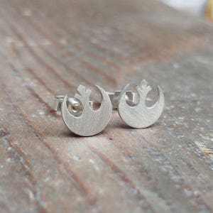 May include: A pair of silver Rebel Alliance symbol stud earrings. The earrings are small and delicate, and they are perfect for anyone who loves Star Wars.