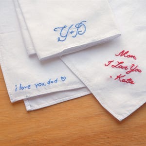 May include: Three white fabric handkerchiefs featuring embroidered text. One displays blue cursive initials Y+D, another has blue text reading i love you, dad with a heart, and the third features red cursive text reading Mom, I Love You - Katie.