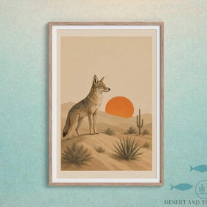 May include: Framed art print featuring a coyote in a desert landscape. The artwork depicts a coyote standing on a dune, with a setting orange sun and desert plants. The print is in a wooden frame.