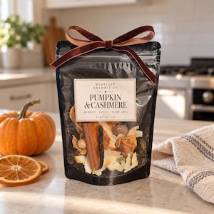 May include: A clear plastic pouch containing dried ingredients for a simmer pot, topped with a brown velvet ribbon. The label reads Midnight Bramble Co, Pumpkin & Cashmere, pumpkin, vanilla, warm spice, simmer pot. Visible contents include cinnamon sticks.