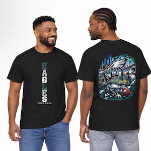 Puede incluir: Una camiseta negra con un gráfico vertical blanco y verde azulado de 'EAGLES FOOTBALL' en el frente. La parte posterior muestra una ilustración detallada del horizonte de Filadelfia, el logo del equipo, un casco y un balón con 'EAGLES'.