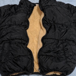 May include: Black puffer jacket with a tan fleece lining. The jacket is unzipped, revealing the soft interior. The outer material has a quilted design. The jacket appears to be a winter coat.