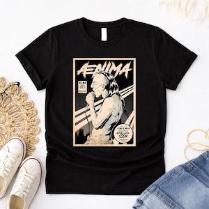 May include: Black t-shirt featuring a comic book-style graphic with the word "Aenima" at the top. The graphic depicts a person holding a microphone. The text "End is Near Armageddon Soon" is also visible. The shirt has a crew neck.