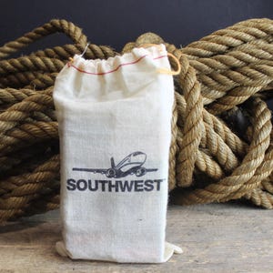 May include: A white fabric pouch with a red drawstring and the Southwest Airlines logo printed on the front. The pouch is sitting on top of a pile of brown rope.