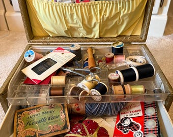 May include: A vintage sewing box with a yellow interior, filled with various sewing supplies including spools of thread, a red tomato-shaped pincushion, a Handy Dandy needle case, Singer needle packets, and packages of self-cover buttons.