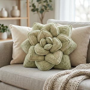 May include: A decorative, sage green, succulent-shaped pillow rests on a gray sofa, surrounded by neutral-toned throw pillows. The succulent pillow has a textured, crocheted appearance, adding a unique touch to the home decor.