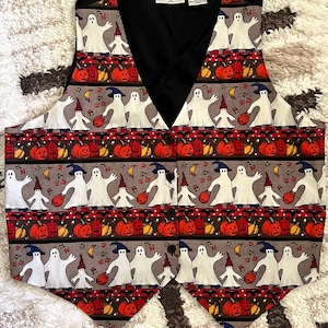 May include: A sleeveless vest featuring a repeating Halloween pattern of white ghosts wearing blue and red hats, orange jack-o'-lanterns, and small bats on a brown background. The vest has a black V-neck collar, a button-front closure, and a label reading Basic Editions.