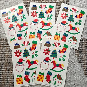 May include: Five sheets of Christmas-themed stickers. Each sheet features Santa Claus, a rocking horse, Christmas trees, stockings, gift boxes, and houses. The stickers are in red, green, yellow, and white.