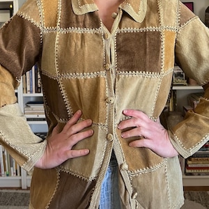 May include: A vintage patchwork jacket in shades of brown and tan. The jacket features a button-up front, a collar, and long sleeves. The design includes square and rectangular patches with decorative stitching.