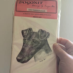 May include: A package of notecards featuring a detailed black and white drawing of a Fox Terrier. The package includes the text "DOGONIT" and "Drawings by Monique Akar". The notecards are described as "8 French Fold Notes with Envelopes".