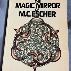May include: A vintage book titled "The Magic Mirror of M.C. Escher" by Bruno Ernst. The cover features a detailed illustration of three brown snakes encircling a complex geometric design in shades of green and white. The book's title is in bold black letters.