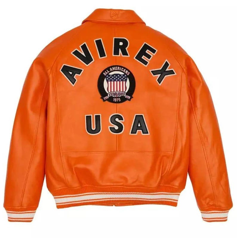 May include: Bright orange leather jacket with the word "AVIREX" arched across the top and "USA" at the bottom. A circular patch in the centre features the words "ALL AMERICANS" and "ESTABLISHED 1975" around a red, white, and blue emblem. The jacket has white and black striped cuffs.