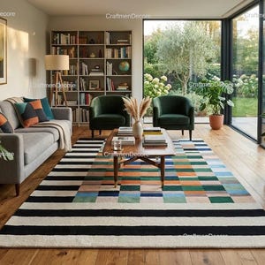 May include: A living room scene featuring a gray sofa with colorful throw pillows, two green armchairs, and a wooden coffee table. A large rug with black and white stripes and colorful squares covers the floor. The room has a large window overlooking a garden.