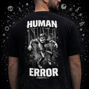 May include: Black t-shirt with a distressed graphic of a puppet-like figure suspended by strings. The words "HUMAN ERROR" are printed above and below the illustration in a bold, white font. The shirt has a vintage, worn look.