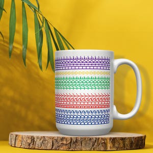 May include: A white ceramic mug featuring a series of horizontal bands with geometric patterns in purple, yellow, green, red, and blue. The mug has a standard handle on the right side and is positioned upright on a circular wooden base.
