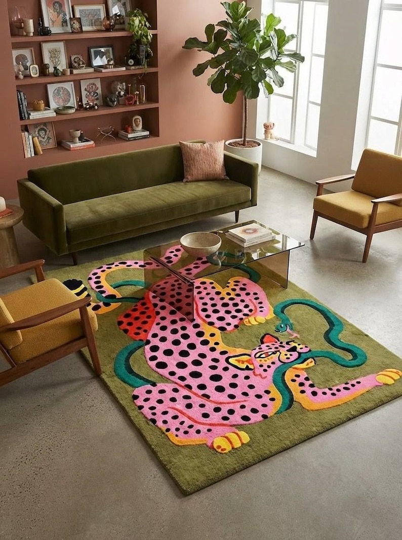 Peut inclure: Un tapis rectangulaire orn&eacute; d'un grand l&eacute;opard rose &agrave; pois noirs et d'un long serpent vert s'enroulant autour de son corps. Le tapis pr&eacute;sente un fond vert olive et est plac&eacute; sur un sol en b&eacute;ton devant un canap&eacute; en velours vert.