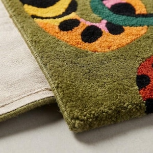 Peut inclure: Un tapis tuft&eacute; pr&eacute;sentant une base vert olive profond avec un motif vibrant de formes jaunes, orange, roses et rouges accentu&eacute;es par des taches noires. Le tapis a un poil &eacute;pais et textur&eacute; avec un bord fini et un envers en tissu beige.