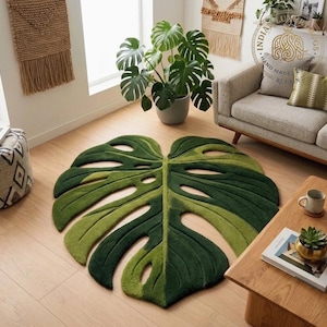 May include: A large, floor-covering rug shaped like a Monstera leaf, featuring a gradient of deep forest green and lighter lime green tones. The rug has a textured, tufted surface with cutouts that mimic the natural fenestrations of a leaf.