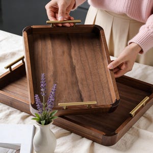 Może przedstawiać: Biały ceramiczny kubek z czarnym uchwytem i napisem "But First, Coffee" pogrubioną, czarną czcionką. Kubek jest ustawiony na rozmytym tle, sugerującym przytulne otoczenie.