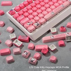 Puede incluir: Un teclado mecánico rosa y blanco con teclas rosas. Las teclas presentan letras blancas y diseños de Hello Kitty. El teclado está rodeado de teclas sueltas con el mismo diseño. El texto "129 Cute Kitty Keycaps MOA Profile PBT Material" es visible.