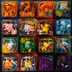 Puede incluir: Una colección de dieciséis teclas de resina cuadradas, cada una con un personaje Pokémon colorido diferente. Las teclas presentan varios Pokémon, incluidos Pikachu, Charizard y Squirtle, en una variedad de poses y colores. Las teclas están dispuestas en un patrón de cuadrícula.