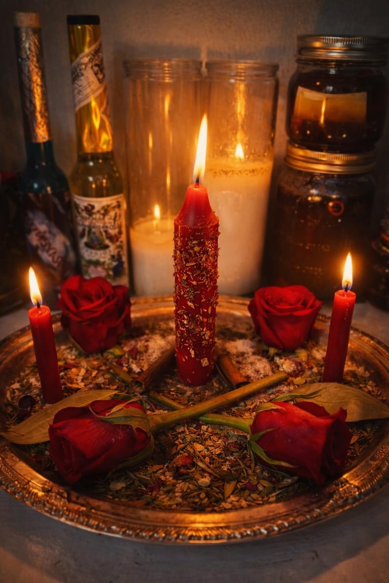 May include: A spiritual altar setup featuring a central red candle adorned with gold flakes, surrounded by red roses, smaller red candles, and herbs on a gold tray. Lit candles and jars create a warm, inviting ambiance.