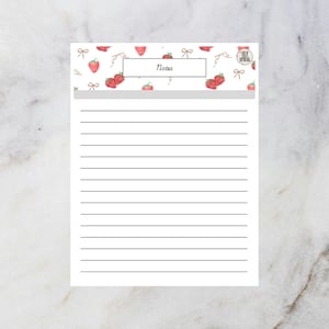 Puede incluir: Un bloc de notas rayado con un patrón de fresas y lazos en la parte superior. El bloc de notas tiene la palabra "Notes" en un recuadro. El fondo es blanco con efecto mármol.