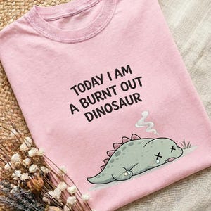 Burnt out dinosaur graphic on pink Comfort Colors shirt with soft cozy lifestyle composition
Minimal burnout tee with funny dinosaur illustration shown on ivory cotton shirt with rustic decor