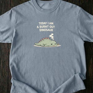 Funny mental health shirt with burnt out dinosaur illustration on blue jean Comfort Colors t-shirt flat lay
Introvert humor burnout tee featuring sleepy exhausted dinosaur design printed on soft cotton shirt