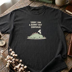 Funny introvert shirt with tired dinosaur design displayed on casual outfit mockup
Burnt out aesthetic shirt with cozy styling and natural textures on rustic wooden surface