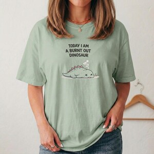 Funny exhausted dinosaur shirt with burnout message styled in natural light flat lay mockup
Mental health awareness shirt with cute dino burnout design printed on soft unisex t-shirt