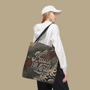 May include: Tote bag with a black shoulder strap and a patterned design. The bag features a mix of animal prints and a brown stripe, with the words "Praise the Lord" in a stylized font.